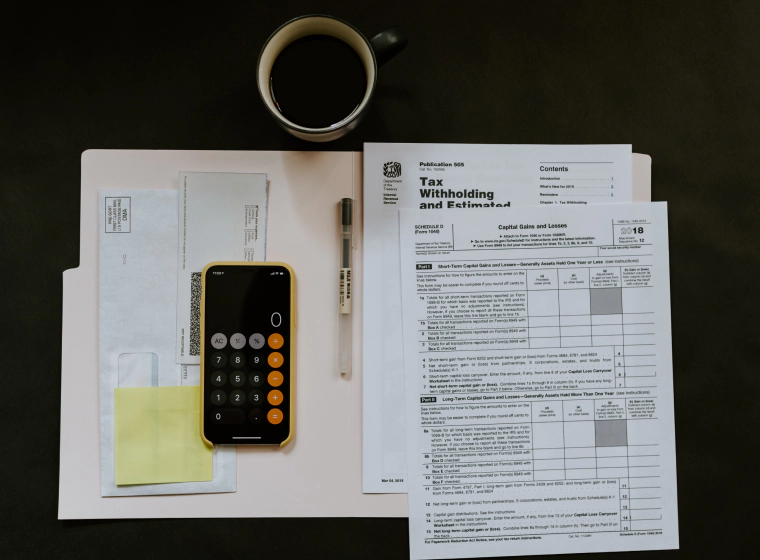 tax papers with a yellow posting a cellphone with the calculator app and a cup of coffee